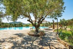 A pool area with a large tree, stone pathway, and outdoor furniture. - Holiday Home 'Simius' with Sea View, Wi-Fi and Air Conditioning (Villasimius)