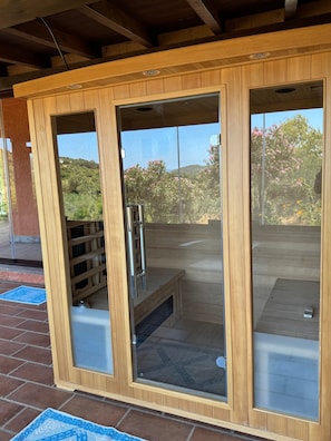 A wooden spa room with glass doors, a metal bench, and a view of a garden. - Holiday Home 'Simius' with Sea View, Wi-Fi and Air Conditioning (Villasimius)