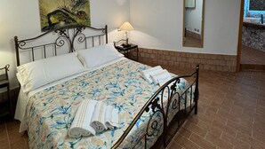 Une chambre à coucher avec un lit, une table de chevet, une lampe, un tableau, un miroir et une vue sur l’extérieur.