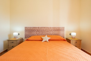 Un lit bien fait, avec une couverture orange, une tête de lit décorative et des lampes de chevet posées sur des tables de nuit en bois.
