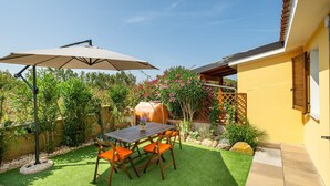 Eine Terrasse mit Tisch und Stühlen, ein Grill und ein gelbes Gebäude mit einer Holztür.