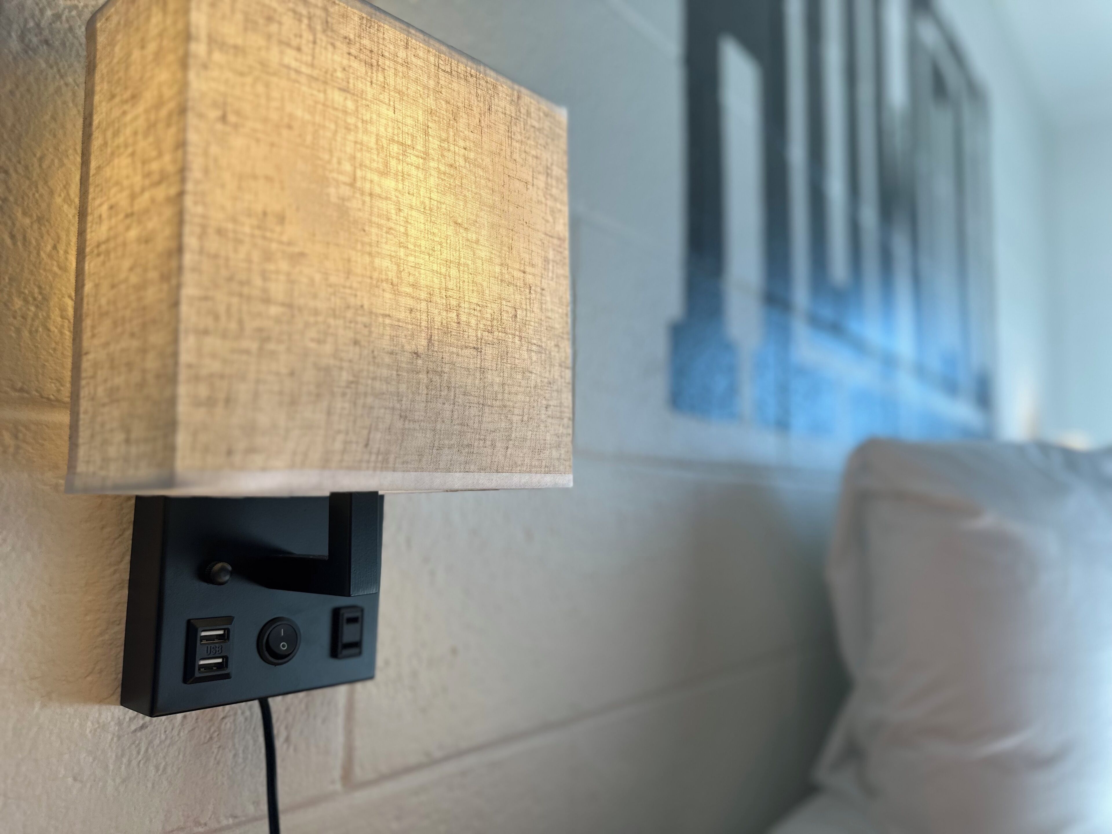 A wall-mounted lamp with a textured shade, a power outlet, and a cable connected to it.