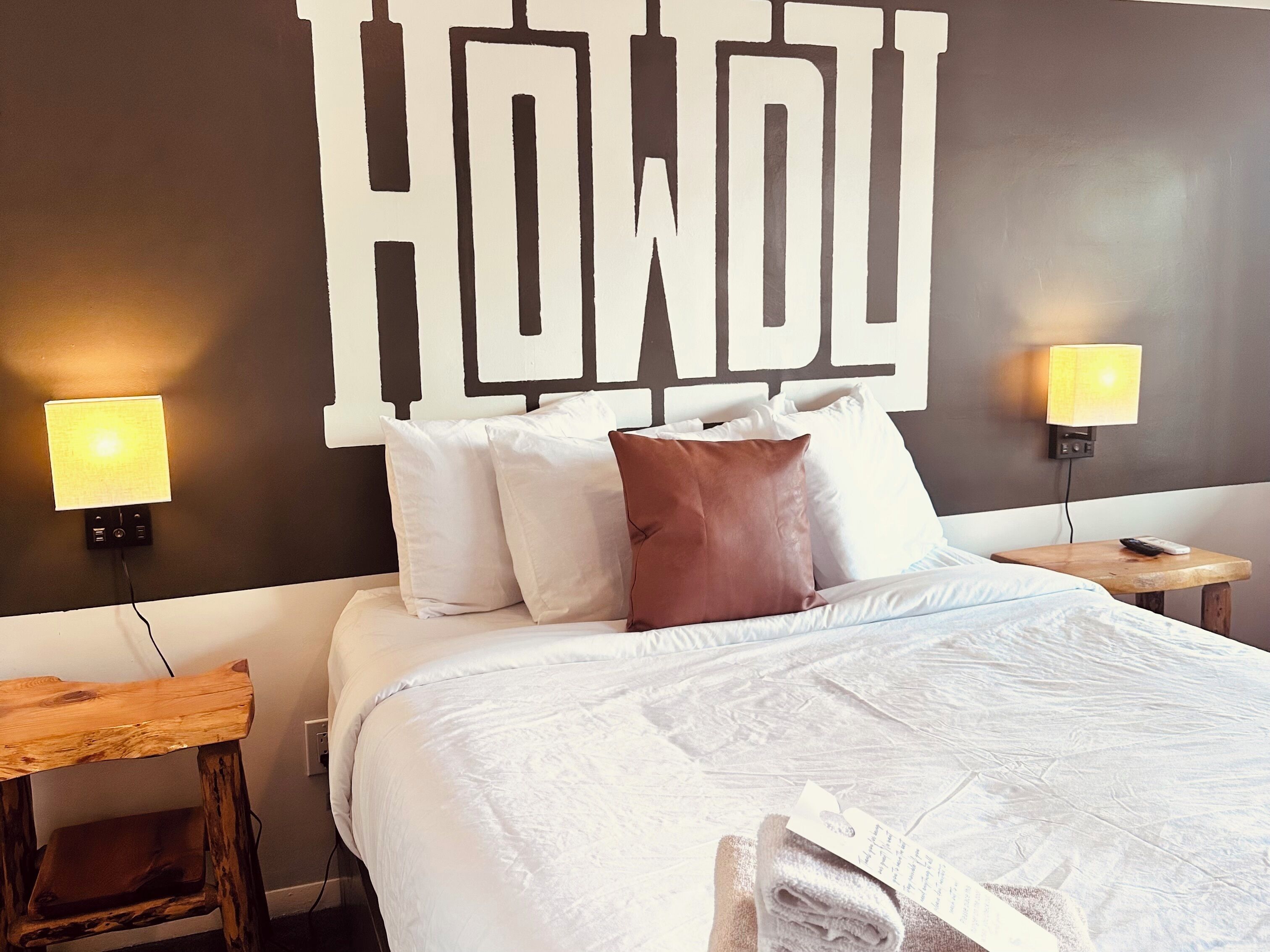 A hotel room with a bed, pillows, a nightstand, and a wall-mounted light fixture.