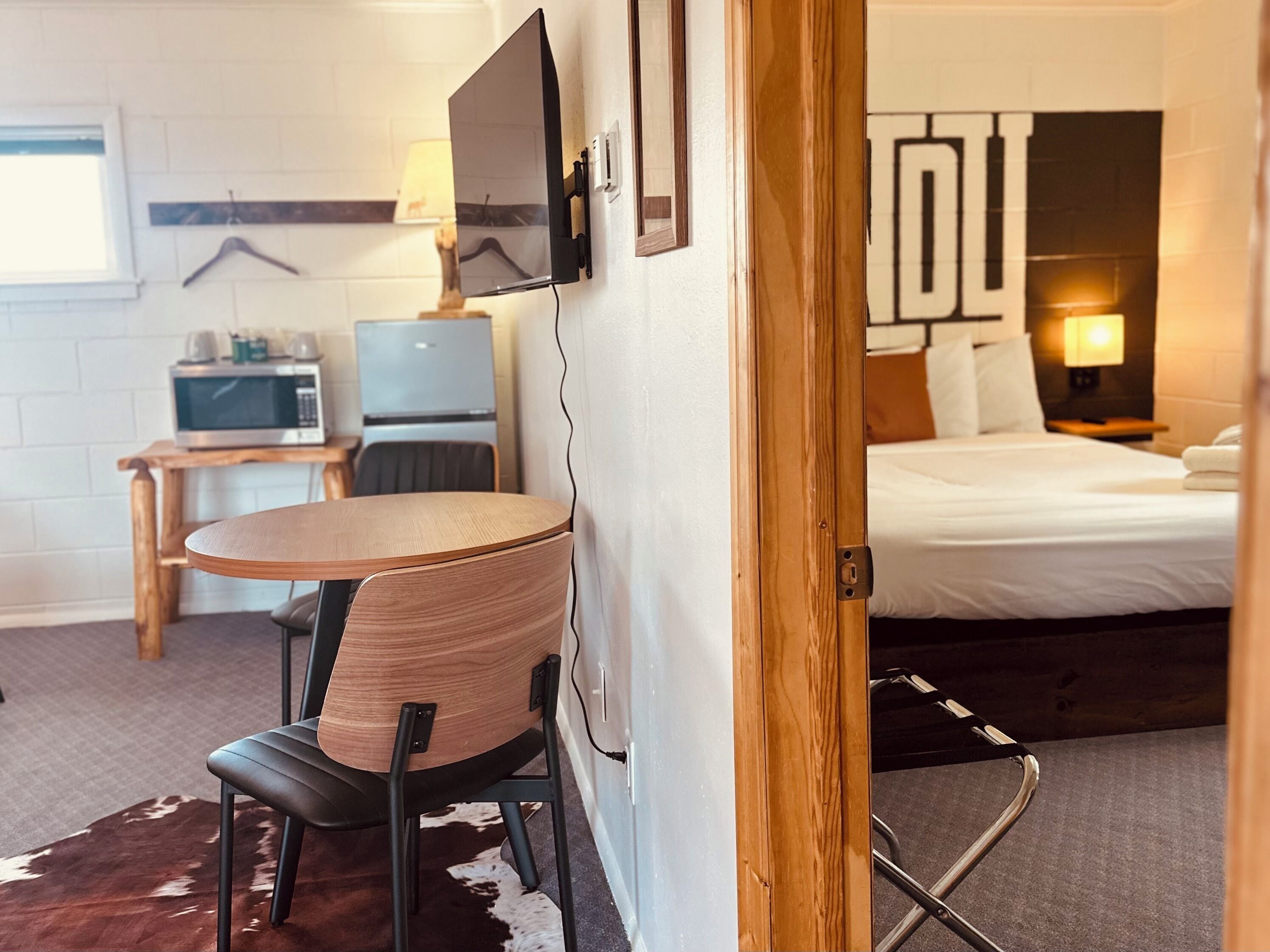 A compact hotel room with a bed, a desk with a computer, a chair, and a small table.