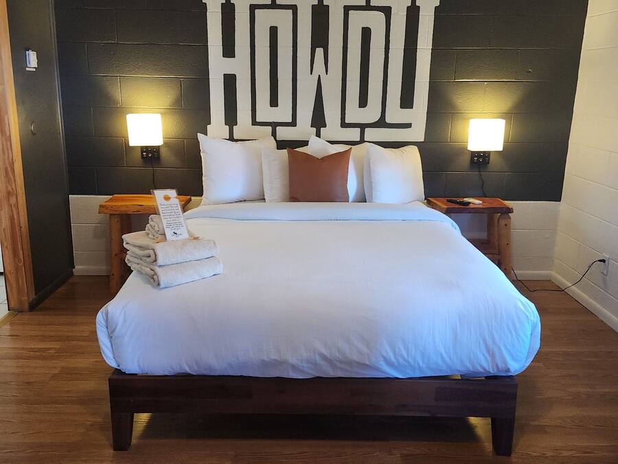 Habitación de hotel con una cama grande, dos mesitas de noche, una lámpara de pared y una obra de arte original en la pared.