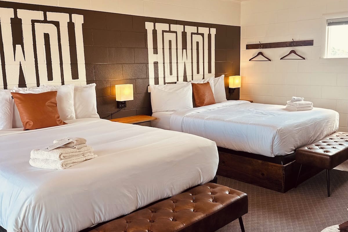 A hotel room with two beds, a bench, a wall-mounted light, and a towel rack.