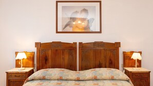 A bedroom with a wooden headboard, two bedside tables with lamps, a floral bedspread, and a framed picture on the wall.