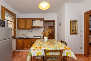 Una cucina con mobili in legno, zoccolo paraschizzi piastrellato, un fornello e un tavolo da pranzo con tovaglia a motivi floreali.