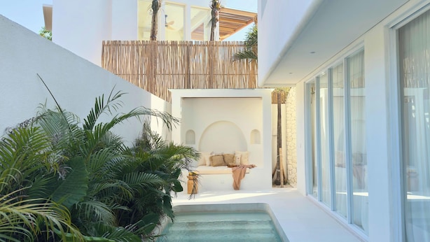 Un área de piscina moderna al aire libre con zona de estar, rodeada de exuberante follaje y paredes blancas.
