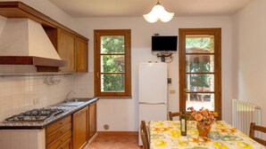 A kitchen with wooden cabinets, a gas stove, a sink, a refrigerator, and a dining table with a vase of flowers. - Apartment 'La Sassetta - Collina' with Private Garden (Bibbona)