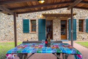 Un edificio de piedra con un patio cubierto, una mesa con mantel colorido y dos botellas de vino.