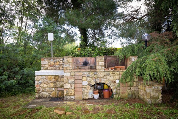 Cocina exterior de piedra con chimenea, rodeada de follaje.