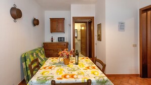 A dining area with a table set for two, a wooden cabinet, and a microwave on the wall. - Apartment 'La Sassetta - Collina' with Private Garden (Bibbona)