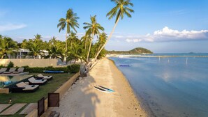 A beachfront hotel with a pool, lounge chairs, and palm trees. - Villa Sai Tai – A Private Haven on the Edge of Paradise (Thong Krut)
