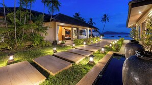 A resort with a pool, palm trees, and a well-lit pathway leading to a building with a beach view. - Villa Sai Tai – A Private Haven on the Edge of Paradise (Thong Krut)