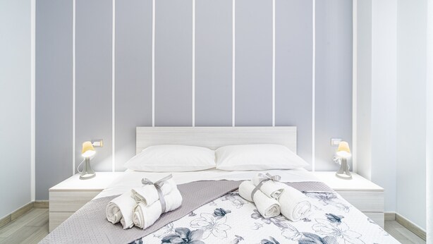 A neatly made bed with pillows, two bedside lamps, and rolled towels on a white nightstand. - Apartment 'Perla  1' with Shared Terrace, Wi-Fi and Air Conditioning (Pachino)