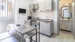 A modern kitchen with a dining area, built-in cabinets, a TV, and a separate bathroom with a mirror. - Apartment 'Perla  1' with Shared Terrace, Wi-Fi and Air Conditioning (Pachino)
