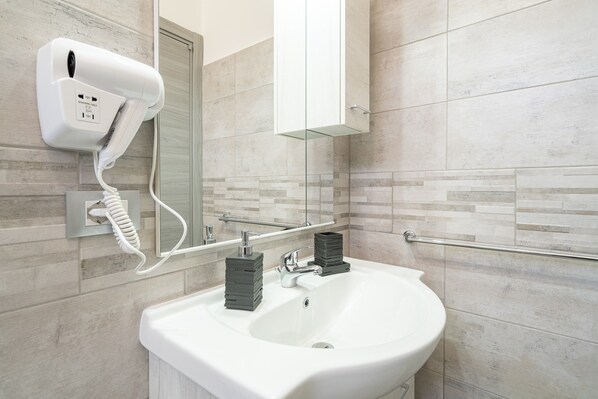 A bathroom with a white sink, a hairdryer mounted on the wall, and a mirror above the sink.