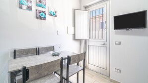 A dining area with a table, chairs, and a television mounted on the wall. - Apartment 'Perla  1' with Shared Terrace, Wi-Fi and Air Conditioning (Pachino)