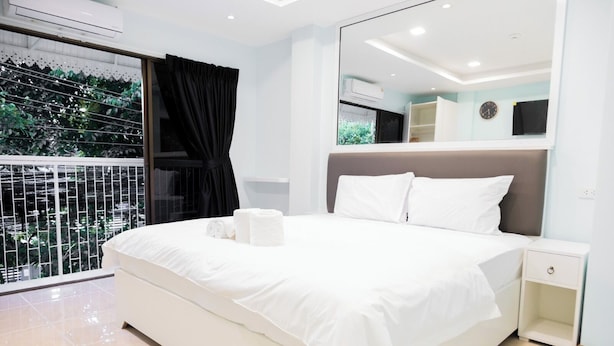 A modern bedroom with a large bed, white bedding, a nightstand, and a mirror. - COZY STAY INN (Bangkok)