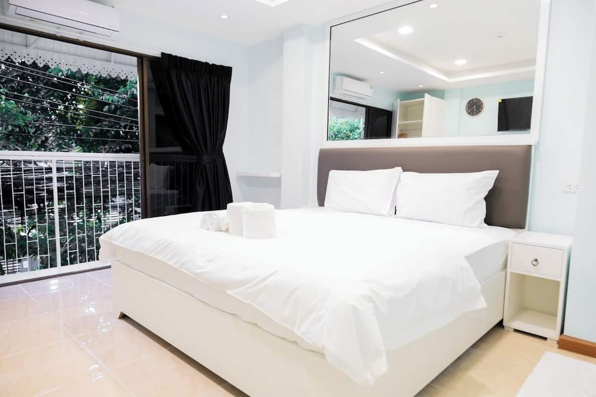 A modern bedroom with a large bed, white bedding, a nightstand, and a mirror.