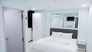 A hotel room with a bed, a bedside table, a wardrobe, a mirror, and an air conditioning unit. - COZY STAY INN (Bangkok)