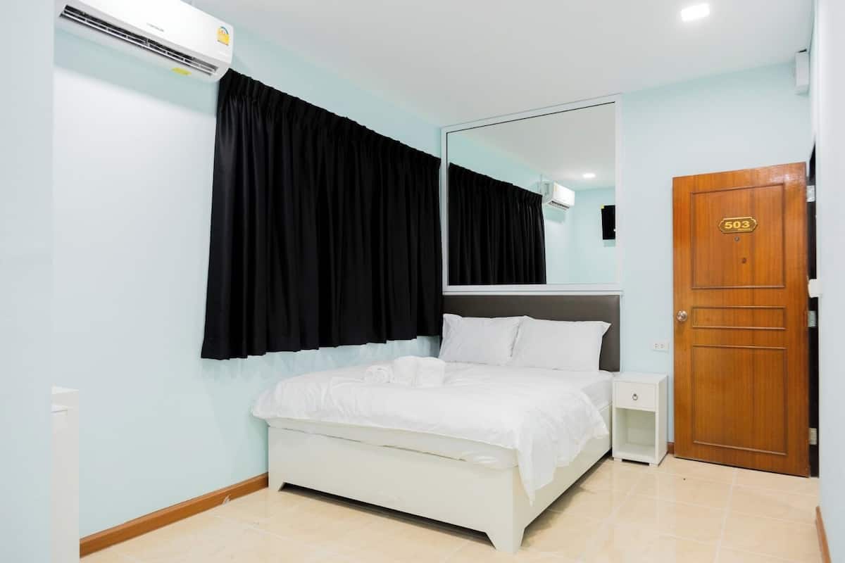 A hotel room with a bed, a nightstand, a mirror, a door, and an air conditioning unit.