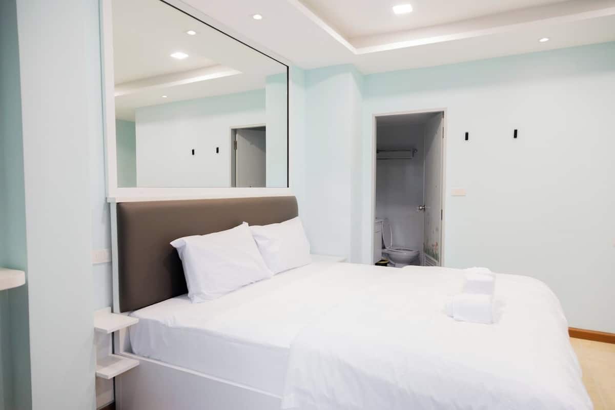 A modern bedroom with a bed, a large mirror, and a walk-in closet.