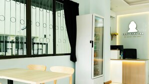 A cozy stay inn with a reception desk, a refrigerator stocked with beverages, and a dining area with a table and chairs. - COZY STAY INN (Bangkok)