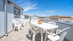 A rooftop terrace with a white table and chairs, a window, and a view of the cityscape.