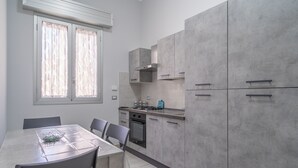 A modern kitchen with grey cabinets, a dining table with chairs, and a window with blinds.