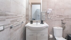 A bathroom with a sink, mirror, towel rack, toilet, and a hairdryer mounted on the wall.
