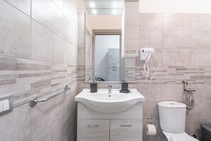 Un baño con lavamanos, espejo, toallero, inodoro y un secador de pelo fijado en la pared.