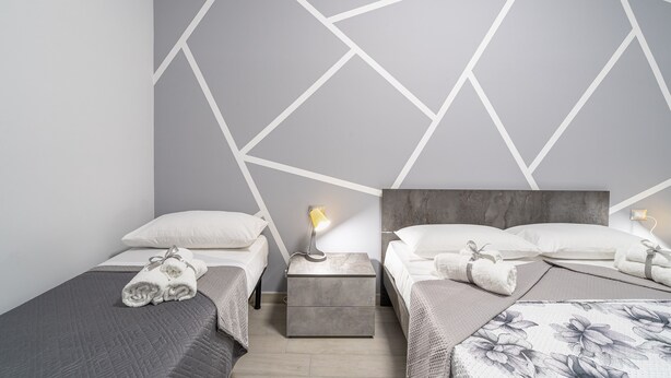 A modern hotel room with two beds, a nightstand with a lamp, and a geometric wall design.