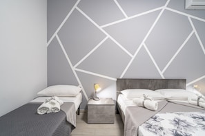 A modern hotel room with two beds, a nightstand with a lamp, and a geometric wall design.