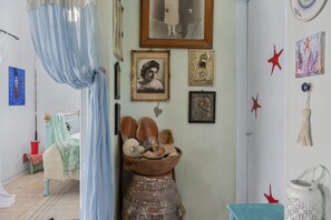 Una habitación con cama, un estante en la pared decorado con objetos y una ventana con cortinas.