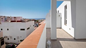 A rooftop terrace with a view of the sea, white buildings, and a clear sky.