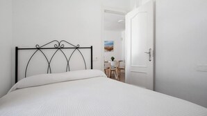 A bed with a metal headboard, a white door, and a small table with chairs in the background.