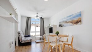 A compact living space with a dining area, a sofa, a ceiling fan, and a painting on the wall.