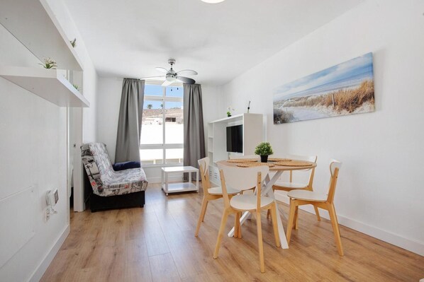 A compact living space with a dining area, a sofa, a ceiling fan, and a painting on the wall.