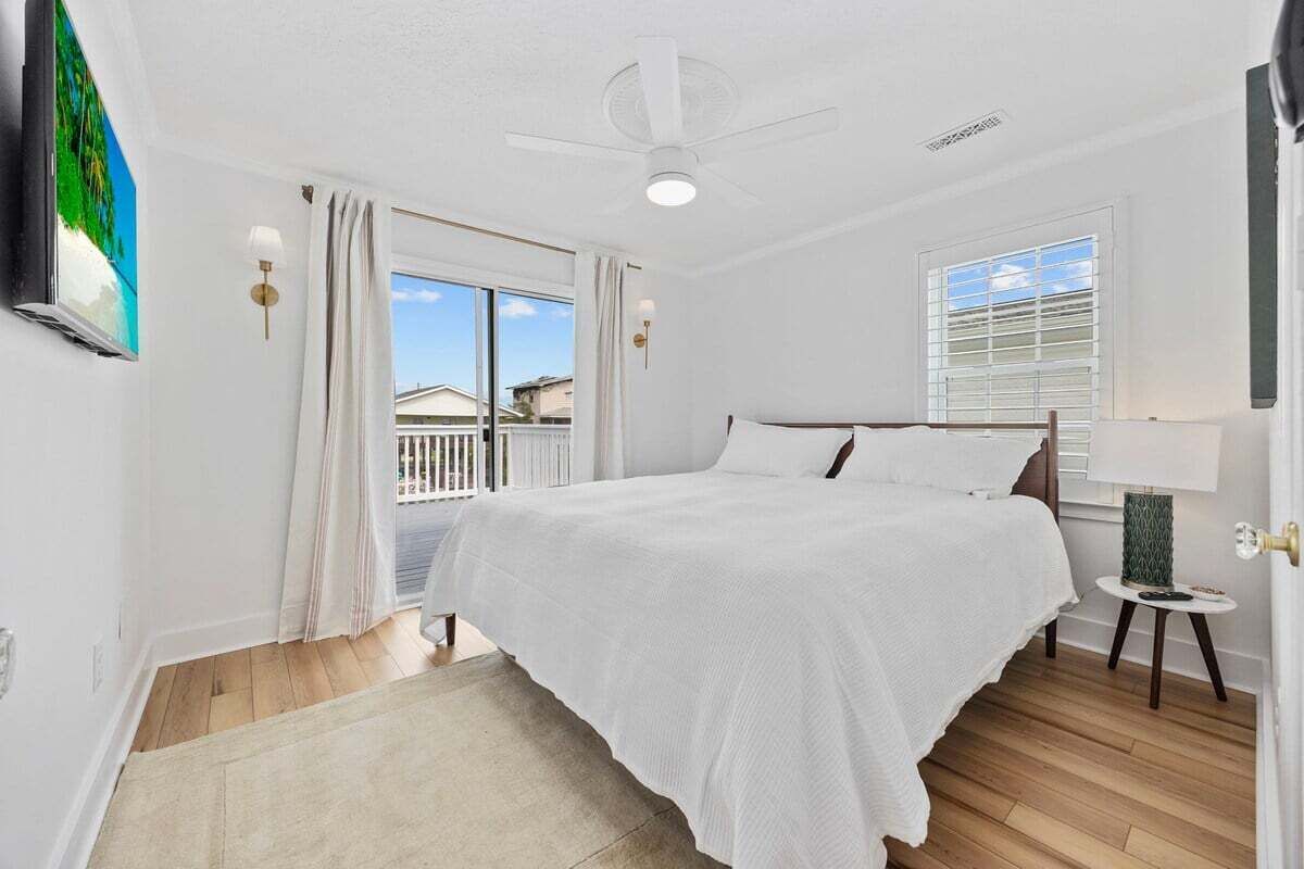 A bedroom with a bed, a ceiling fan, a window with blinds, and a view of the outside.