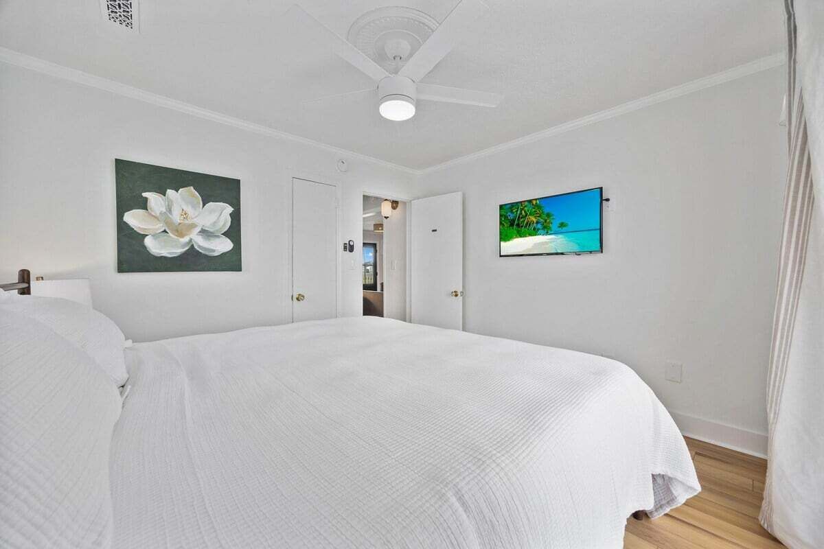 Un dormitorio con cama, ventilador de techo, un cuadro de una flor y televisor en la pared.