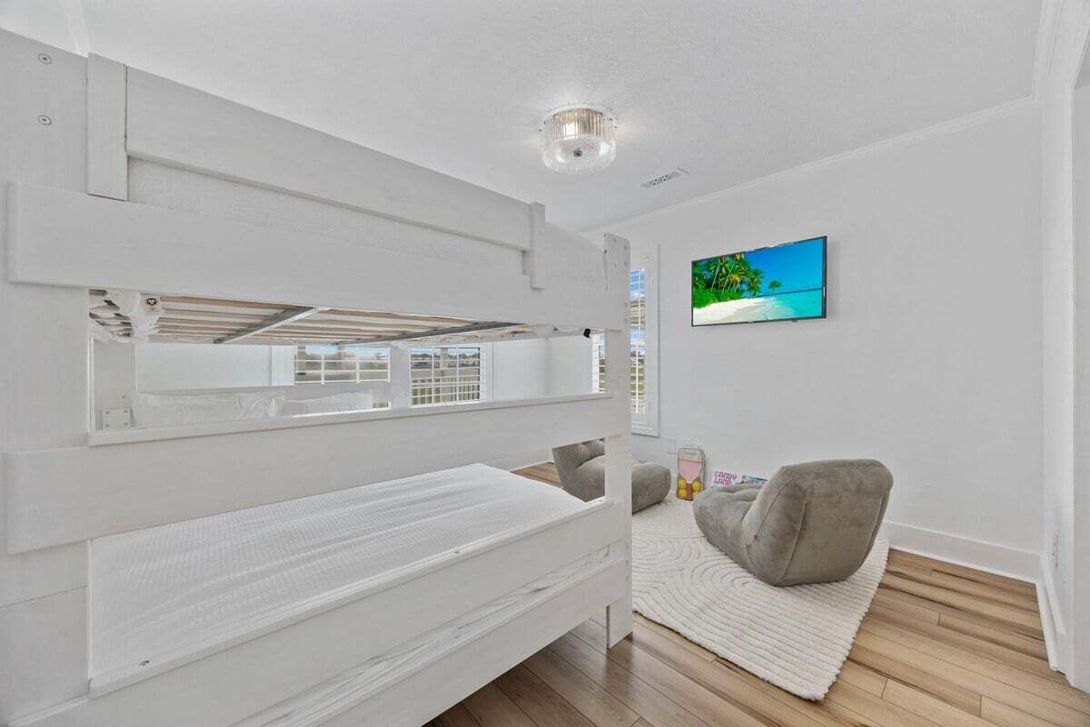 A modern bedroom with a bunk bed, a flat-screen TV on the wall, and a grey chair.