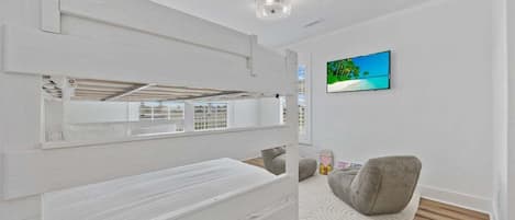 A modern bedroom with a bunk bed, a flat-screen TV on the wall, and a grey chair.