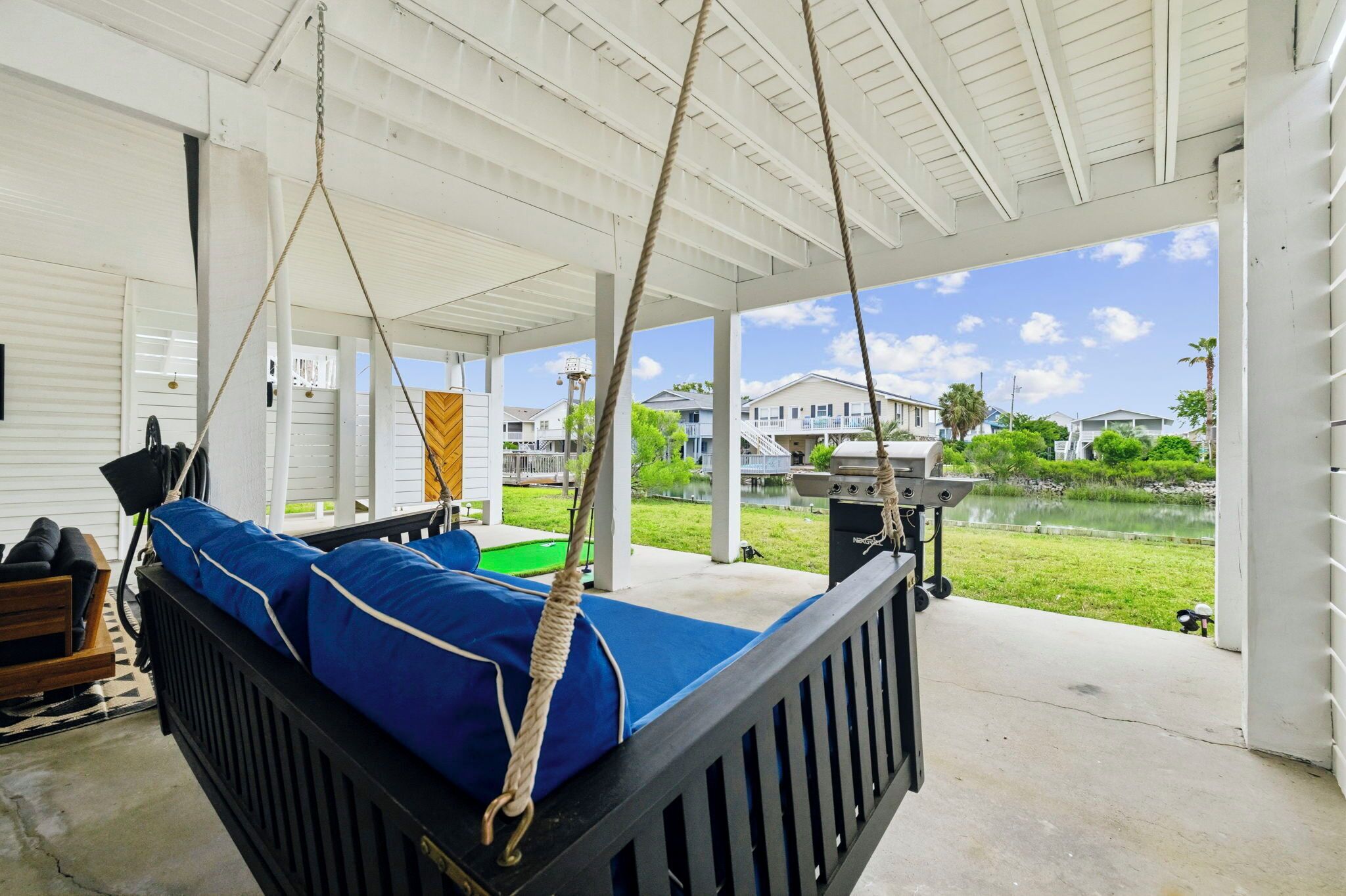 A covered porch with a swing bed, a grill, and a view of a lake and houses.