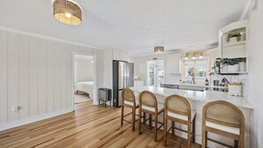 Een moderne keuken met een centraal eiland, houten stoelen, een koelkast en een spoelbak.