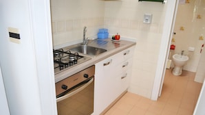 A kitchen with a gas stove, sink, and oven, and a bathroom with a toilet and sink.