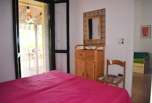 Ein Zimmer mit einem Bett, einem Holzschrank, einem Stuhl, einem Spiegel und Blick durch eine Tür.