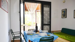 A dining area with a table set for four, chairs, a sofa, and a view through an open door.