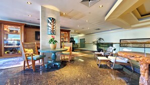 A lobby with a marble floor, seating area with chairs and a table, a potted plant, and a large wall art piece.